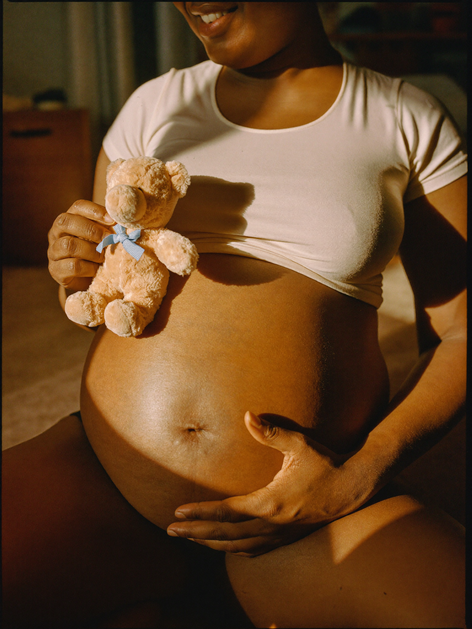 Gestante brasileira segurando ursinho para o bebê na barriga, expressão de alegria e ternura, representando quem tem direito ao salário maternidade